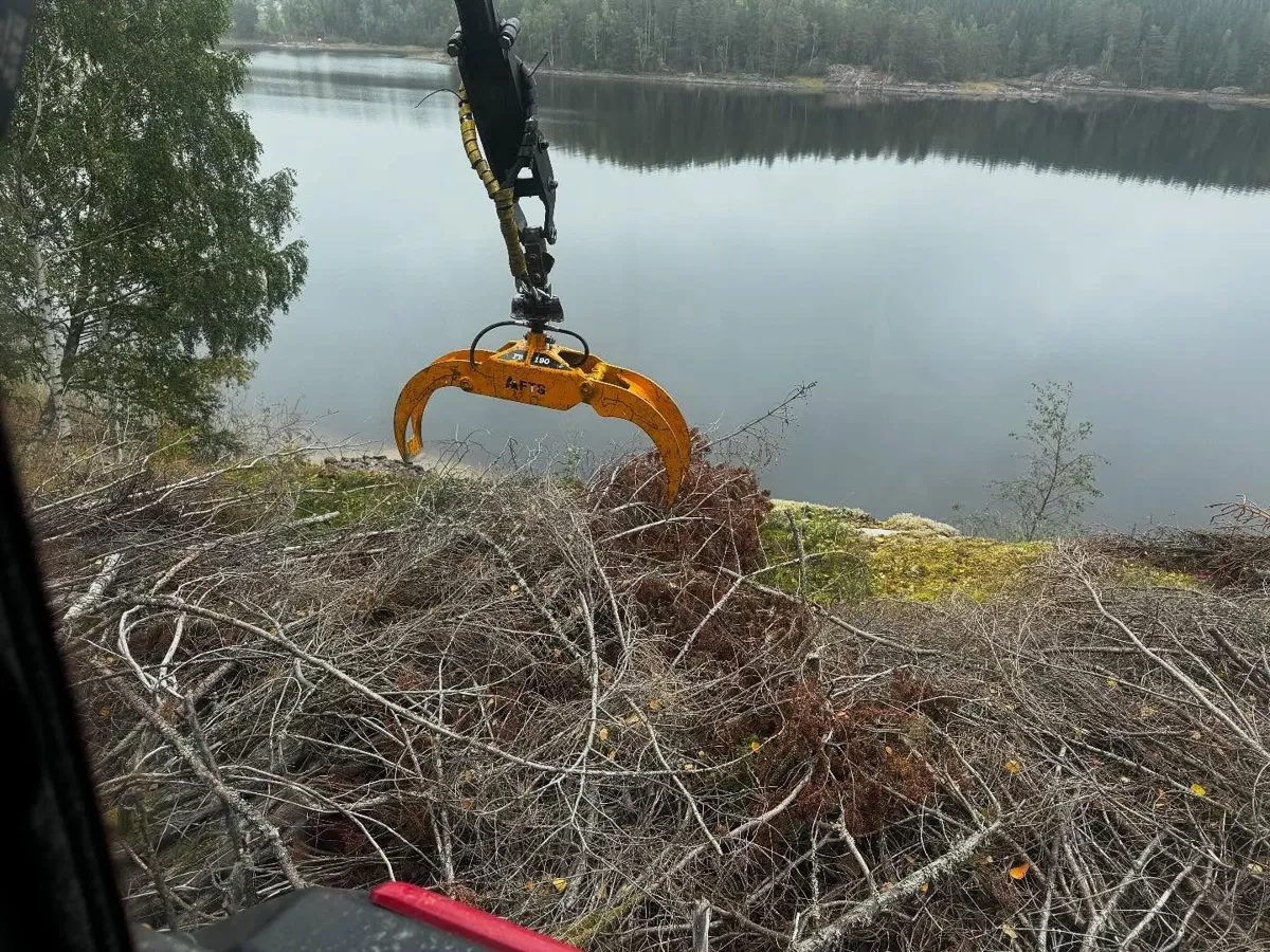 Gripklo över ris vid en spegelblank skogssjö, sett från traktorhytten