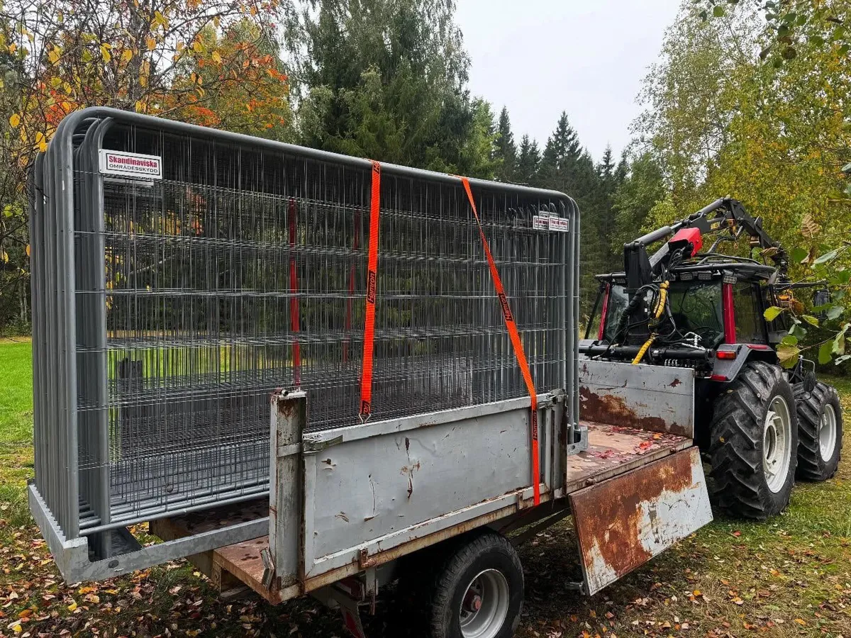 Byggstängsel fastspänt med orange spännband på en tippvagn bakom traktorn